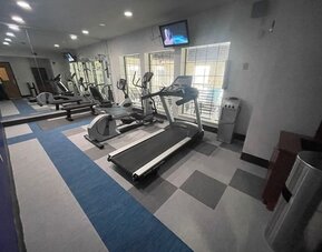 Spacious fitness centre with cardio equipment, mirrored wall, televisions, and large windows at Comfort Suites San Antonio SeaWorld - Lackland AFB.