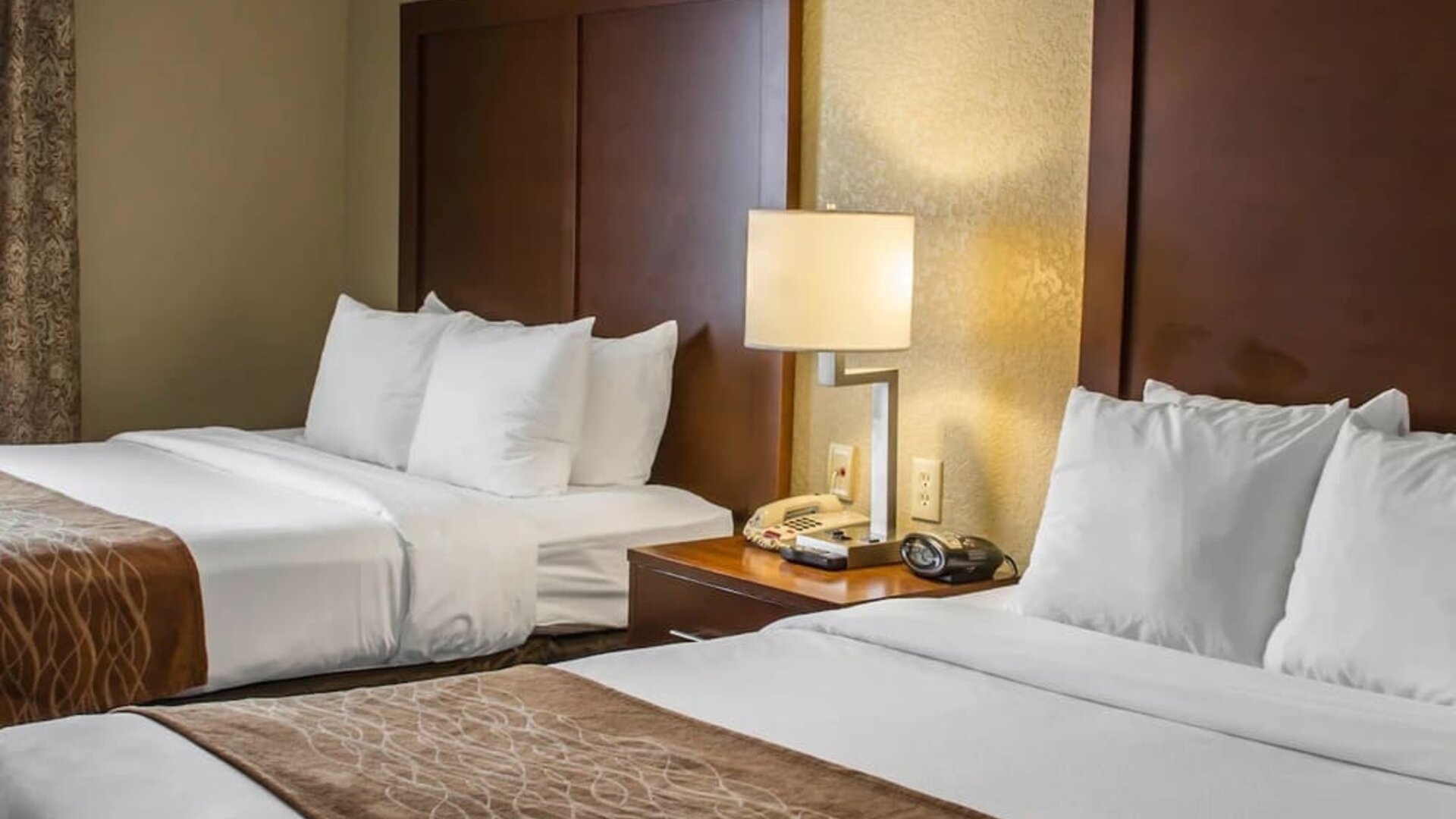 Guest room with two beds, white bedding, wooden headboards, bedside table, lamp, and alarm clock at Comfort Suites San Antonio SeaWorld - Lackland AFB.