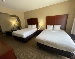 Spacious guest suite with two beds, bedside lighting, and a separate seating area with sofa and ottoman at Comfort Suites San Antonio SeaWorld - Lackland AFB.