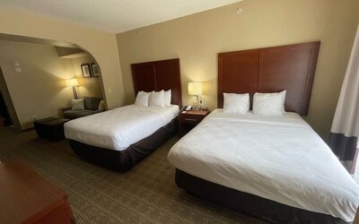 Spacious guest suite with two beds, bedside lighting, and a separate seating area with sofa and ottoman at Comfort Suites San Antonio SeaWorld - Lackland AFB.
