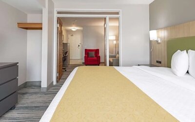 King guest room with white bedding, yellow bed runner, green headboard, and adjoining seating and workspace area at SureStay by Best Western Lewisville Dallas.