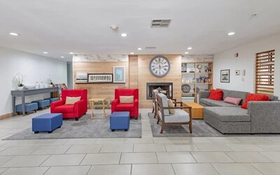 Hotel lobby with sofas, red armchairs, ottomans, fireplace, wall clock, and lounge seating at SureStay by Best Western Lewisville Dallas.