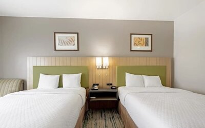 Guest room with two beds, white bedding, green upholstered headboards, shared nightstand, bedside lighting, and framed artwork at SureStay by Best Western Lewisville Dallas.