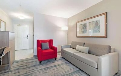 Guest suite seating area with sofa, red armchair, floor lamp, and framed artwork at SureStay by Best Western Lewisville Dallas.