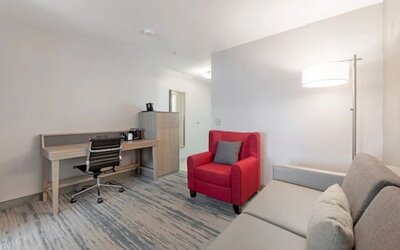 Guest suite workspace with desk, office chair, storage cabinet, red armchair, sofa, and floor lamp at SureStay by Best Western Lewisville Dallas.