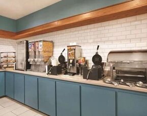 Breakfast station with waffle makers, cereal dispensers, pastries, and hot-food service area at SureStay by Best Western Lewisville Dallas.