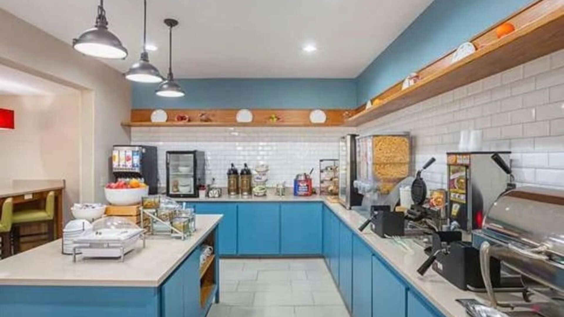 Breakfast buffet with waffle makers, cereal dispensers, hot-food station, beverages, and blue cabinetry at SureStay by Best Western Lewisville Dallas.