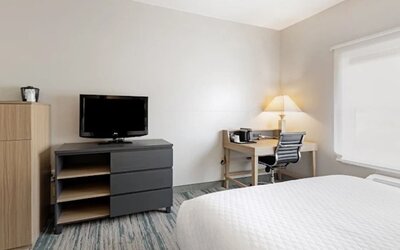 Guest room with television, dresser, work desk, office chair, lamp, and large window at SureStay by Best Western Lewisville Dallas.