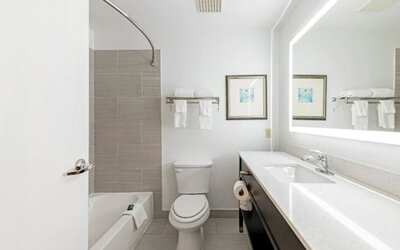 Guest bathroom with bathtub, tiled shower wall, toilet, long vanity, and illuminated mirror at SureStay by Best Western Lewisville Dallas.