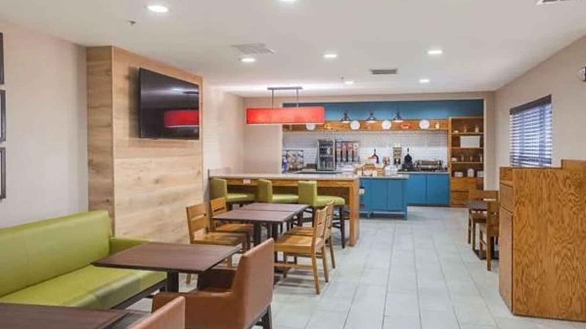 Hotel dining area with tables, chairs, booth seating, television, and breakfast station at SureStay by Best Western Lewisville Dallas.