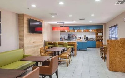 Hotel dining area with tables, chairs, booth seating, television, and breakfast station at SureStay by Best Western Lewisville Dallas.
