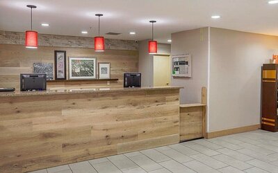Reception area with wood-panelled front desk, red pendant lights, framed artwork, and bookcase at SureStay by Best Western Lewisville Dallas.