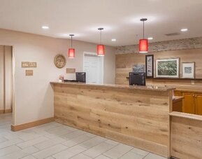 Front desk with wood-panelled reception counter, computer stations, red pendant lighting, and wall décor at SureStay by Best Western Lewisville Dallas.