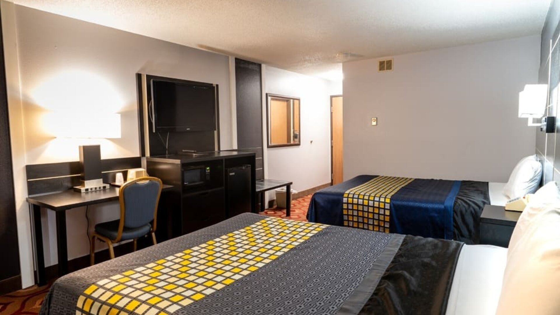 Guest room with two beds, patterned bedding, work desk, television, microwave, and mini refrigerator at Coratel Inn & Suites By Jasper Hastings.