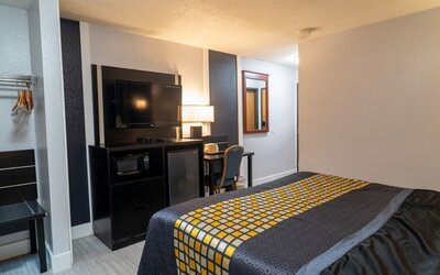 Guest room with bed, television, microwave, mini refrigerator, work desk, and open hanging space at Coratel Inn & Suites By Jasper Hastings.