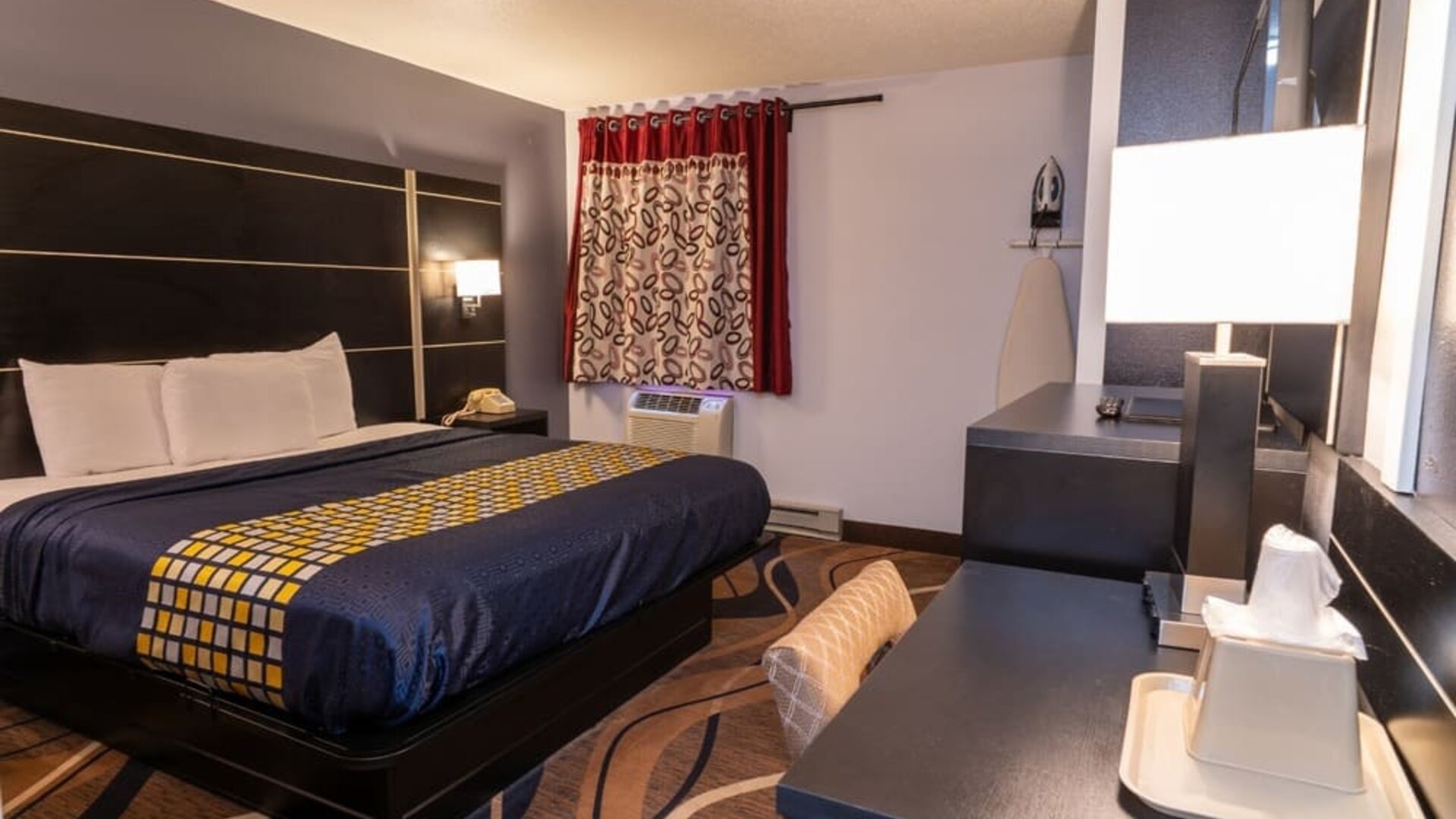 King guest room with patterned bedding, work desk, window, and in-room ironing facilities at Coratel Inn & Suites By Jasper Hastings.