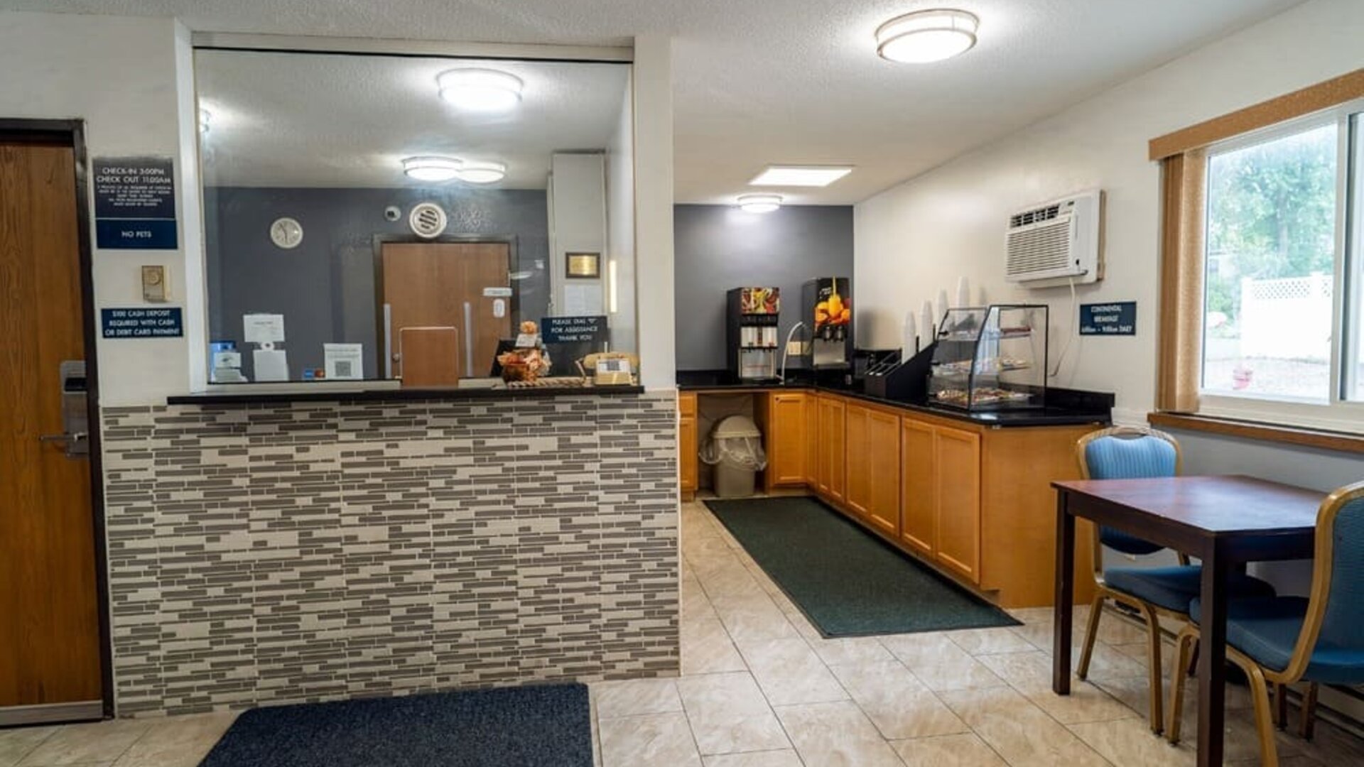 Reception desk beside the breakfast area with dining table, beverage station, and pastry display at Coratel Inn & Suites By Jasper Hastings.