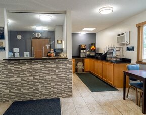 Reception desk beside the breakfast area with dining table, beverage station, and pastry display at Coratel Inn & Suites By Jasper Hastings.