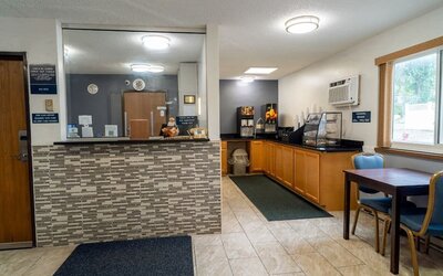 Reception desk beside the breakfast area with dining table, beverage station, and pastry display at Coratel Inn & Suites By Jasper Hastings.
