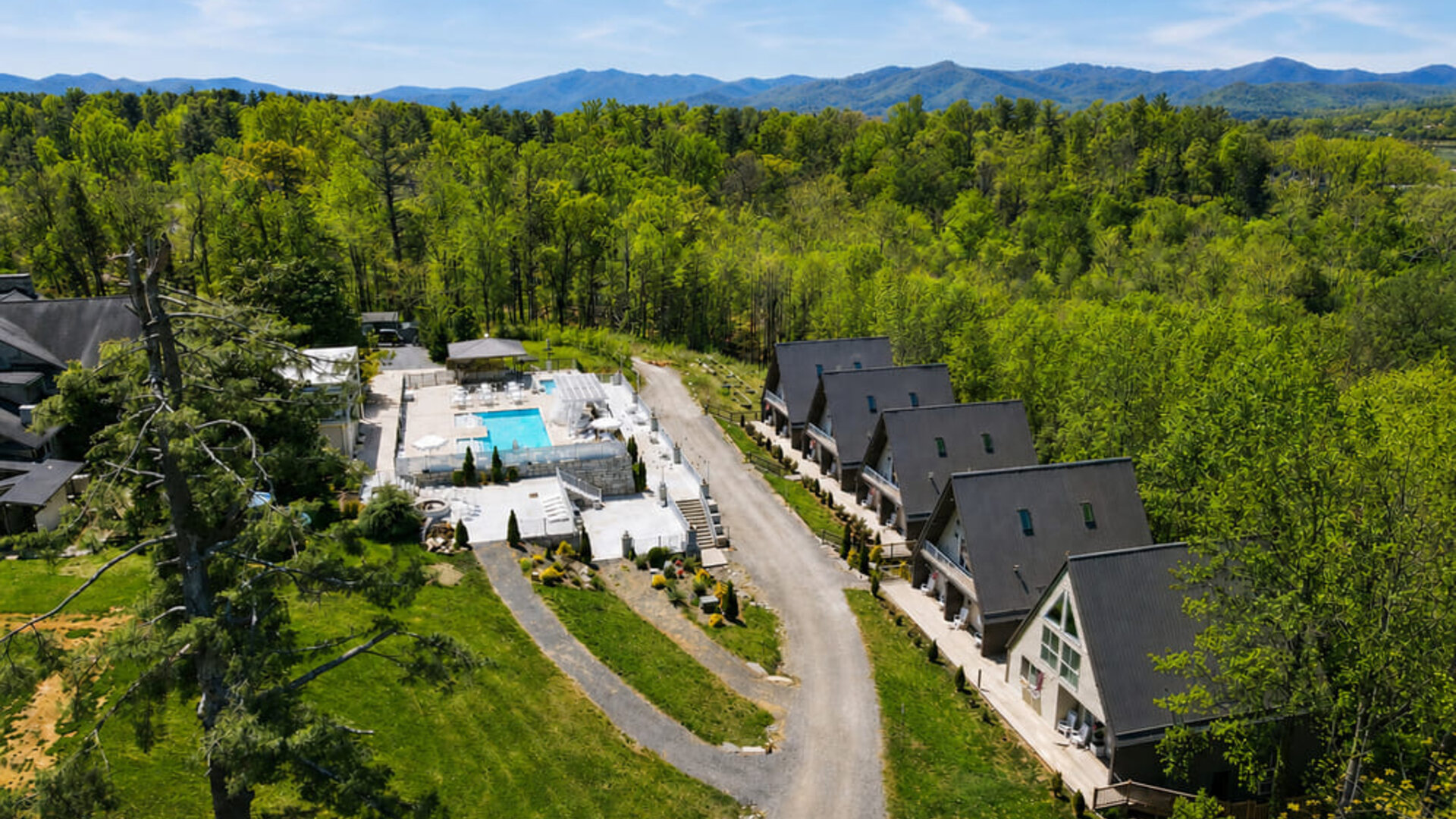Aerial view of SKYLARANNA Resort & Spa, showing the pool complex, chalet-style accommodation, wooded grounds, and surrounding mountain landscape.