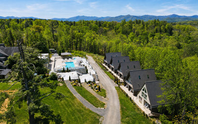 Aerial view of SKYLARANNA Resort & Spa, showing the pool complex, chalet-style accommodation, wooded grounds, and surrounding mountain landscape.