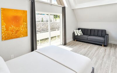 Cabin bedroom and sitting area at SKYLARANNA Resort & Spa, featuring a queen bed, sofa, vaulted ceiling, colourful artwork, and sliding doors providing natural light.