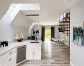 Modern cabin kitchen and open-plan interior at SKYLARANNA Resort & Spa, featuring white cabinetry, an island with sink, dining area, spiral staircase, and contemporary décor.