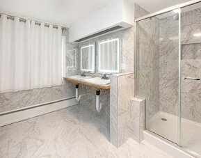 Spacious cabin bathroom at SKYLARANNA Resort & Spa, featuring double sinks, illuminated mirrors, marble-style finishes, and a glass-enclosed shower.