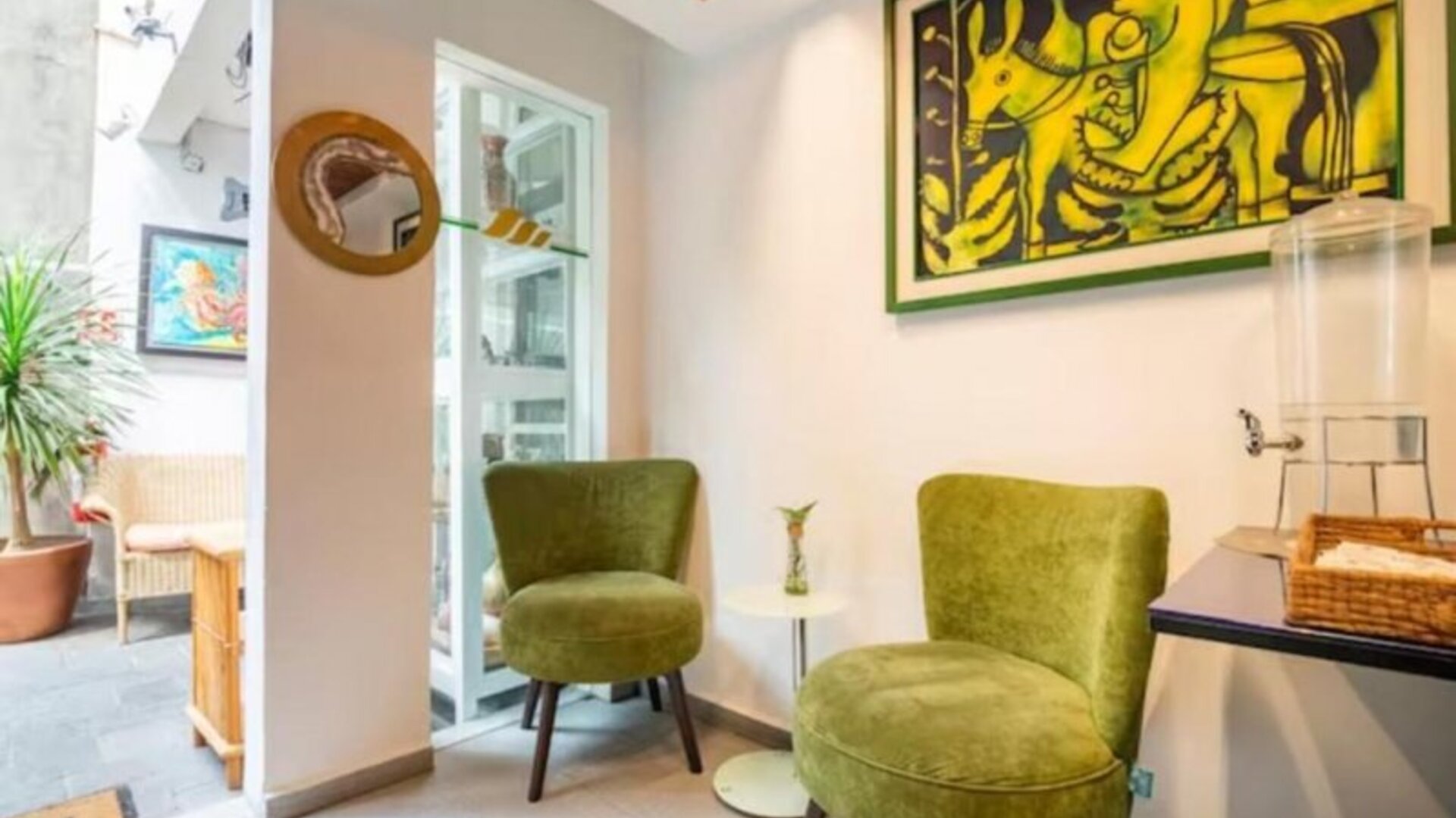 Welcoming common area featuring green lounge chairs, colourful artwork, and a guest refreshment station at Casa Anzures Suites.