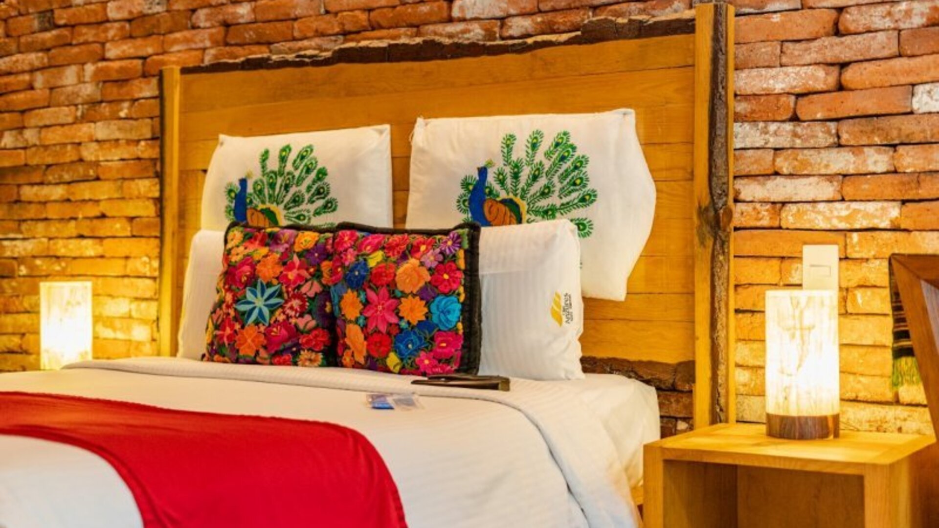 Guest room featuring a large bed, exposed brick accent wall, colourful decorative cushions, and warm bedside lighting at Casa Anzures Suites.