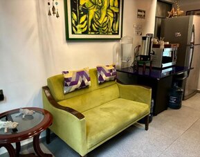 Cosy lounge area featuring a green sofa, decorative cushions, refreshment facilities, and colourful artwork at Casa Anzures Suites.