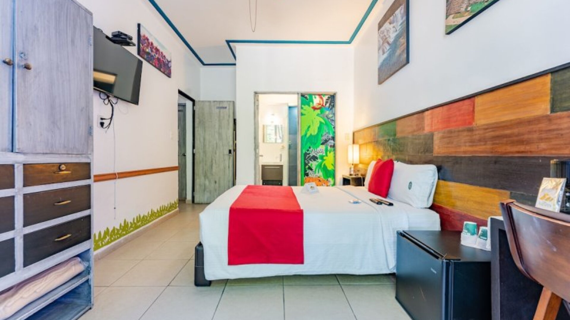 Spacious guest room featuring a large bed, colourful wood-panelled headboard, television, storage, and a desk at Casa Anzures Suites.