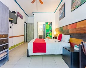 Spacious guest room featuring a large bed, colourful wood-panelled headboard, television, storage, and a desk at Casa Anzures Suites.