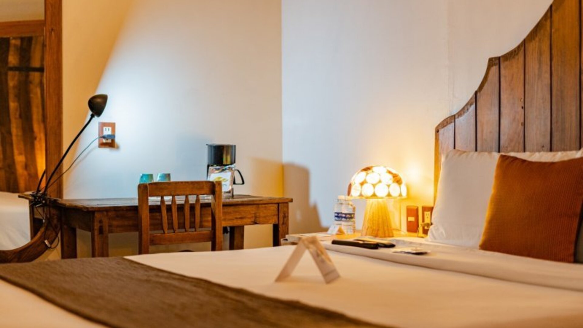 Guest room featuring a comfortable bed, rustic wooden furnishings, bedside lighting, and a dedicated workspace at Casa Anzures Suites.