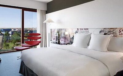 Contemporary guest room featuring a large bed, dedicated workspace, colourful accent seating, and expansive windows with outdoor views at Hilton Madrid Aeropuerto.