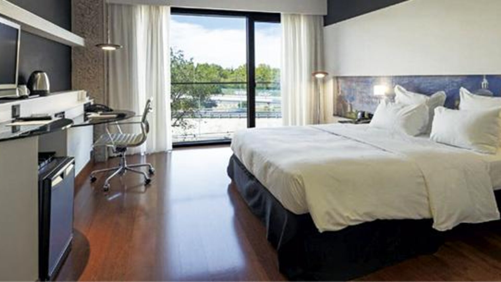 Bright guest room featuring a large bed, television, dedicated workspace, and floor-to-ceiling windows at Hilton Madrid Aeropuerto.