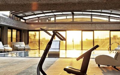 Indoor pool and relaxation area featuring lounge chairs, exercise equipment, and floor-to-ceiling windows at Hilton Madrid Aeropuerto.