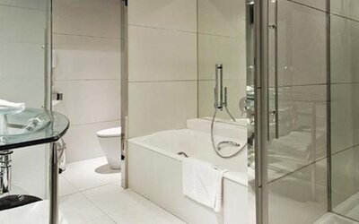 Modern guest bathroom featuring a glass vanity, bathtub, separate glass-enclosed shower, and sleek chrome fixtures at Hilton Madrid Aeropuerto.