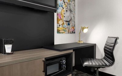 In-room workspace featuring a desk, ergonomic chair, coffee maker, microwave, and contemporary artwork at La Quinta Inn & Suites By Wyndham Cleveland Airport West.