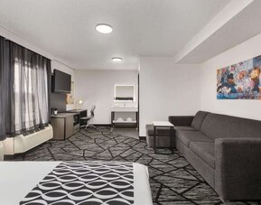 Spacious guest room featuring a bed, sofa seating area, work desk, television, and large windows at La Quinta Inn & Suites By Wyndham Cleveland Airport West.