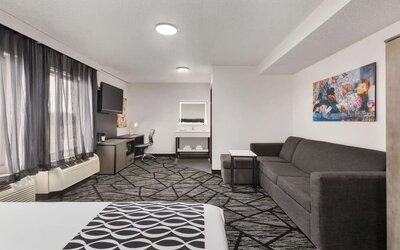 Spacious guest room featuring a bed, sofa seating area, work desk, television, and large windows at La Quinta Inn & Suites By Wyndham Cleveland Airport West.