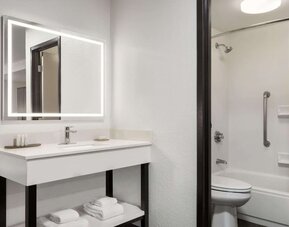 Bright guest bathroom featuring an illuminated mirror, spacious vanity, shower and bathtub combination, fresh towels, and accessibility grab bar at La Quinta Inn & Suites By Wyndham Cleveland Airport West.