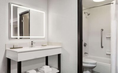 Bright guest bathroom featuring an illuminated mirror, spacious vanity, shower and bathtub combination, fresh towels, and accessibility grab bar at La Quinta Inn & Suites By Wyndham Cleveland Airport West.