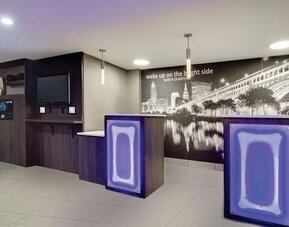 Modern reception area featuring illuminated front desks and a Cleveland cityscape mural at La Quinta Inn & Suites By Wyndham Cleveland Airport West.