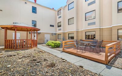 Hotel courtyard with wooden gazebo and raised outdoor terrace featuring tables and chairs beside the guest room building.