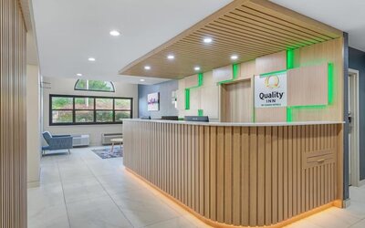 Renovated Quality Inn reception area with modern wood-paneled front desk, green accent lighting, seating area, and large windows.
