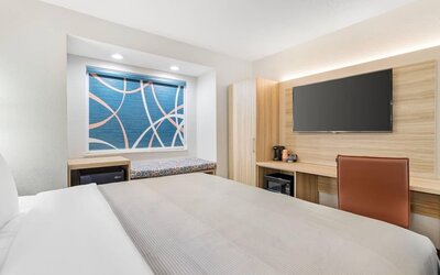 Bright king guest room with teal accent wall, modern wood headboard, white bedding, bedside lighting, desk, and window bench.