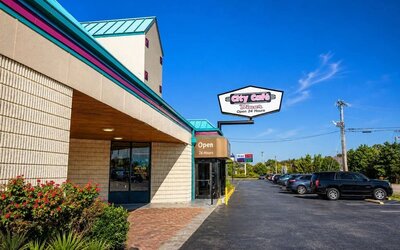 Exterior view of the hotel and City Café entrance with teal roof, landscaped flower beds, City Café roadside sign, and a paved parking area with several vehicles.