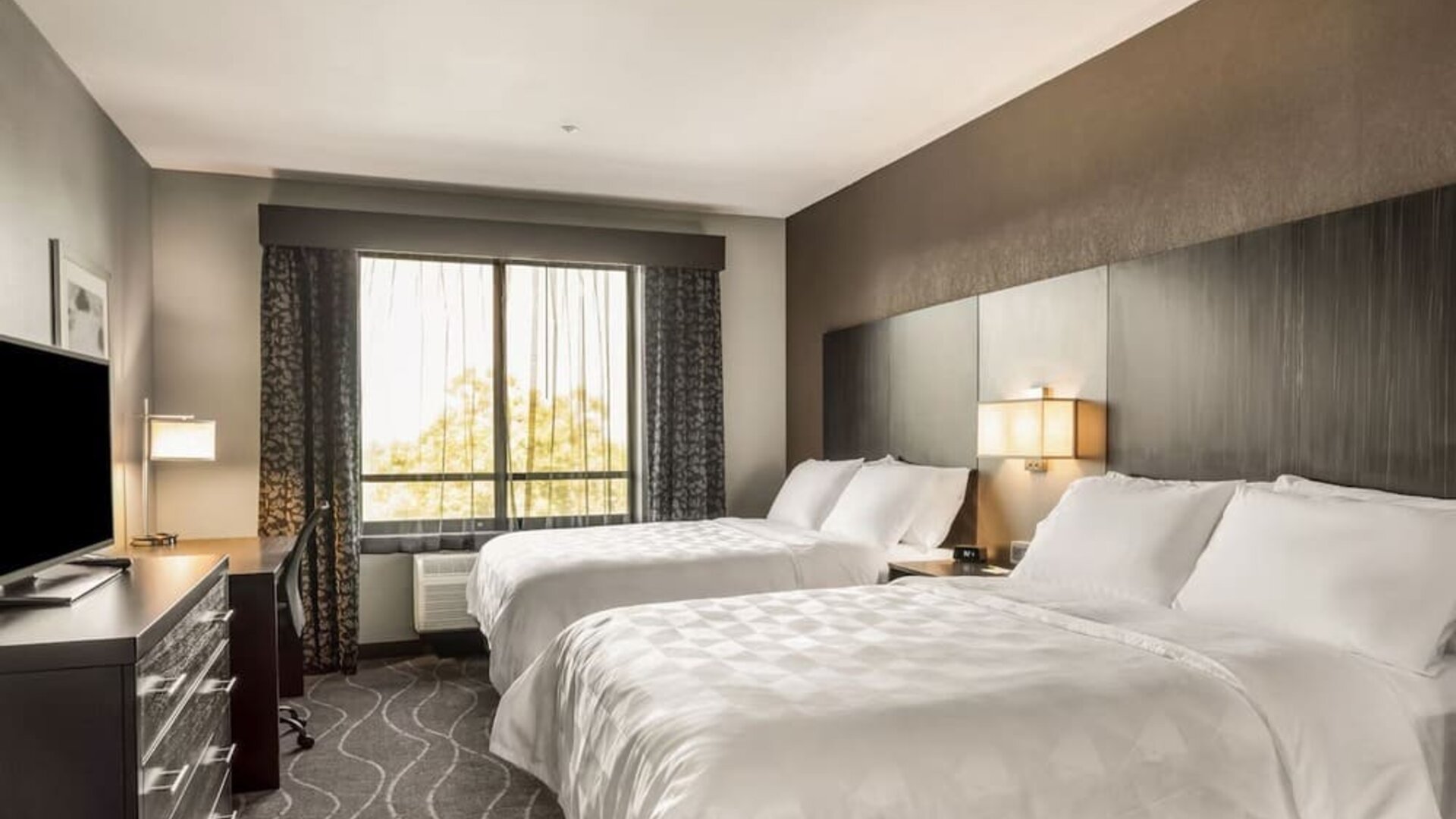 Modern guest room featuring two beds, television, workspace, large window, and contemporary décor at Holiday Inn & Suites Silicon Valley - Milpitas.