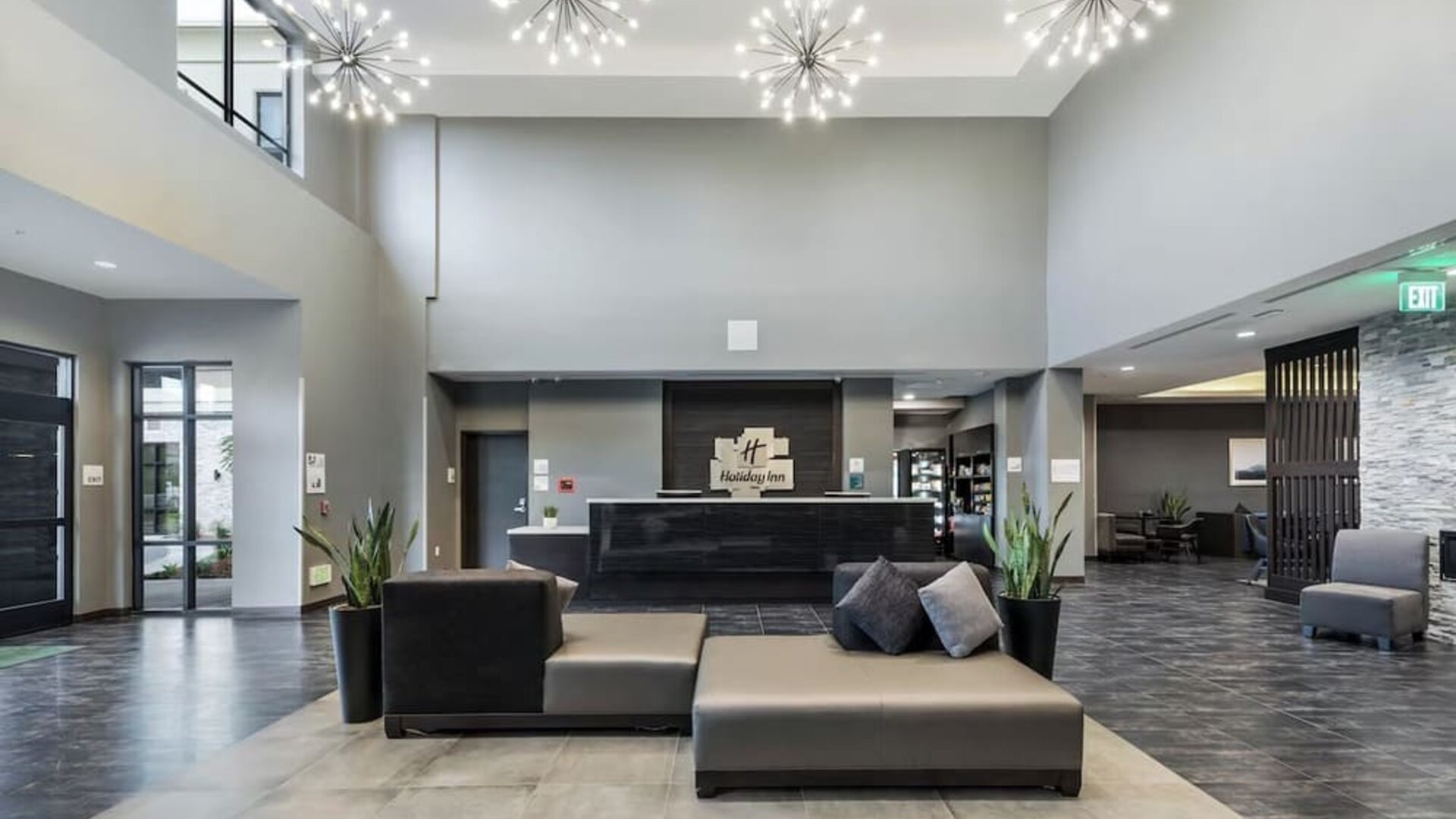 Modern hotel lobby featuring a reception desk, stylish seating, decorative lighting, and an open layout at Holiday Inn & Suites Silicon Valley - Milpitas.